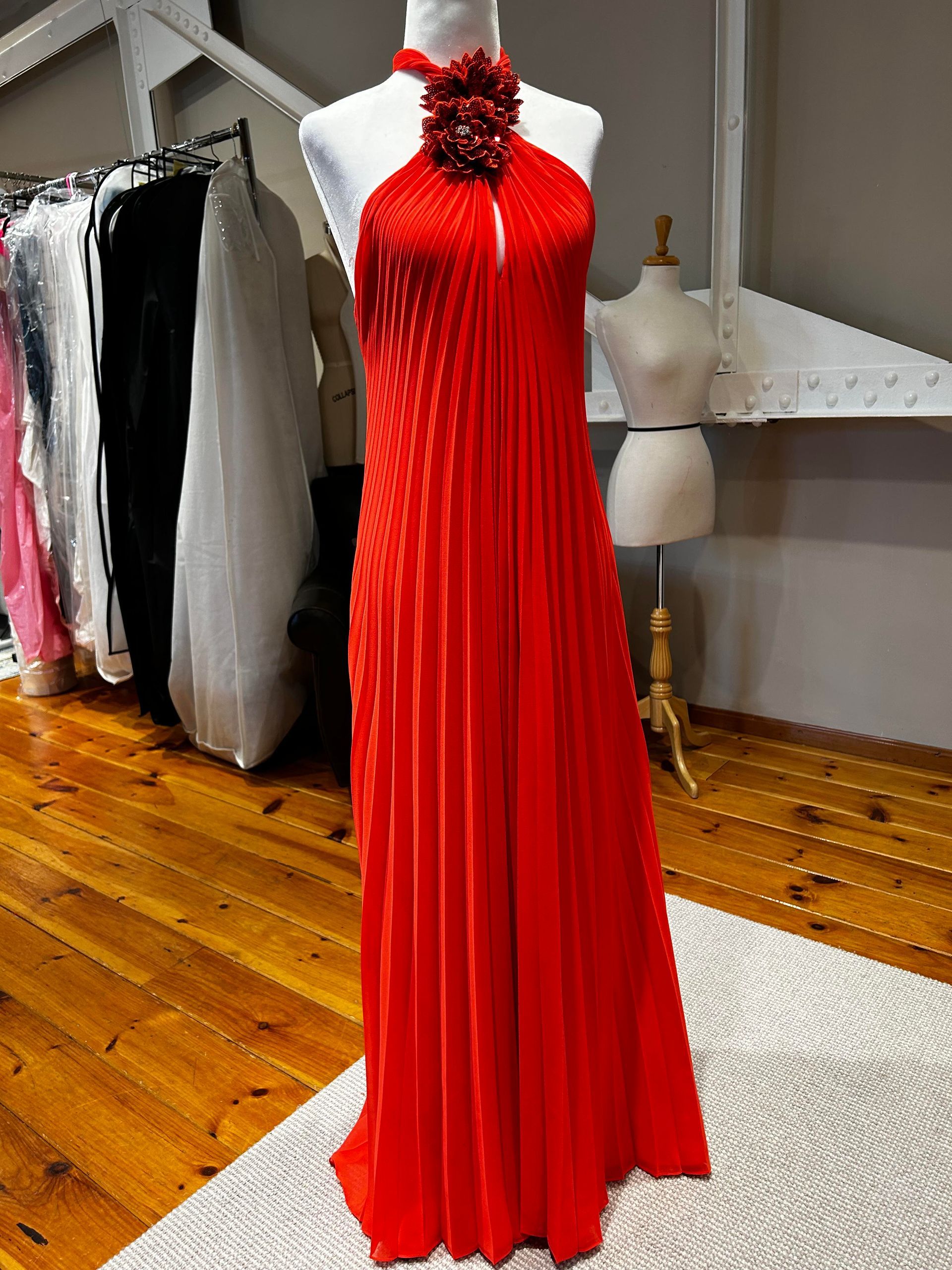 Red halter-neck pleated gown on a mannequin in a clothing studio with hardwood floors