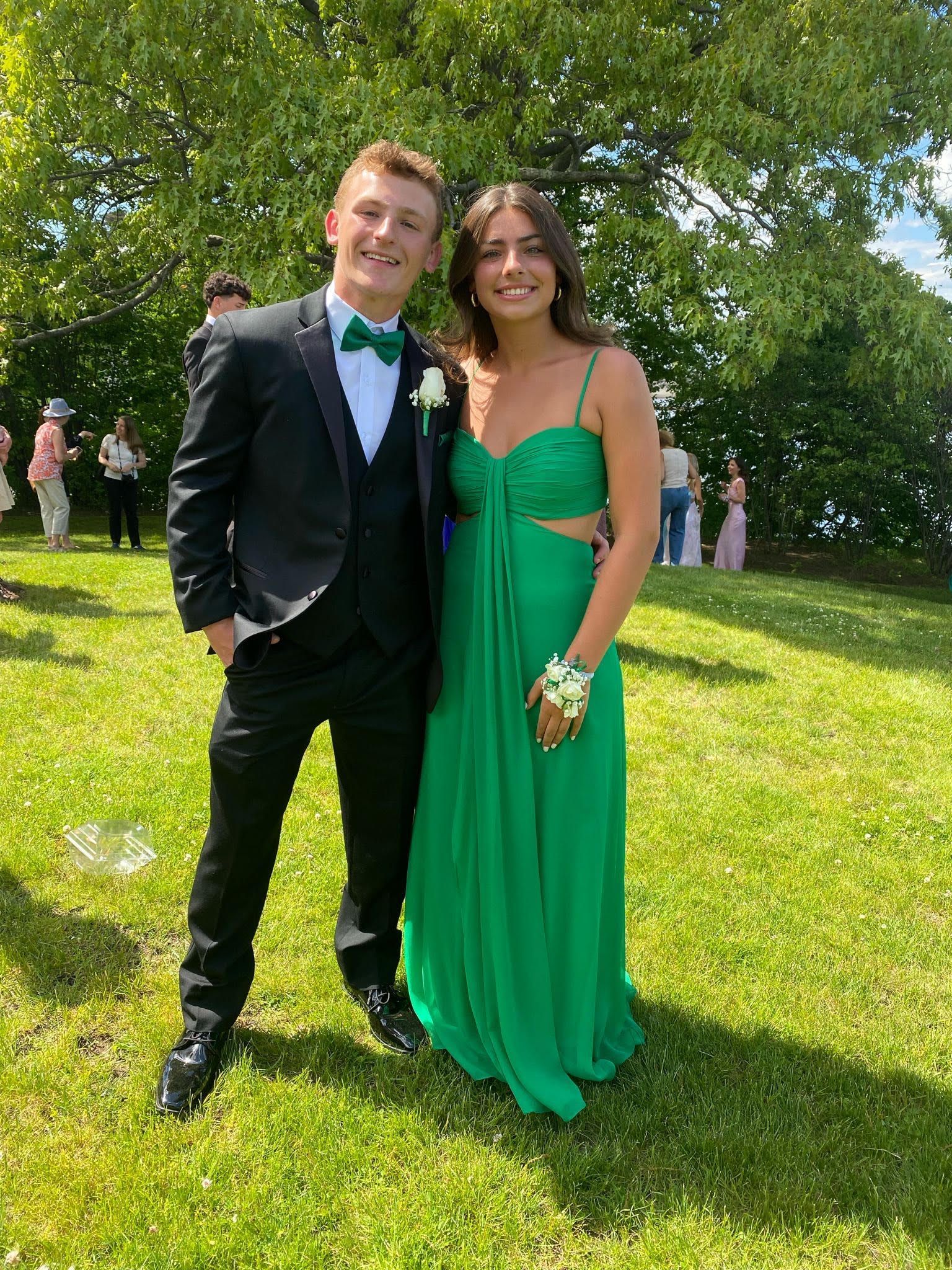 Two people standing on a sunny lawn, dressed for a formal event, smiling at the camera.