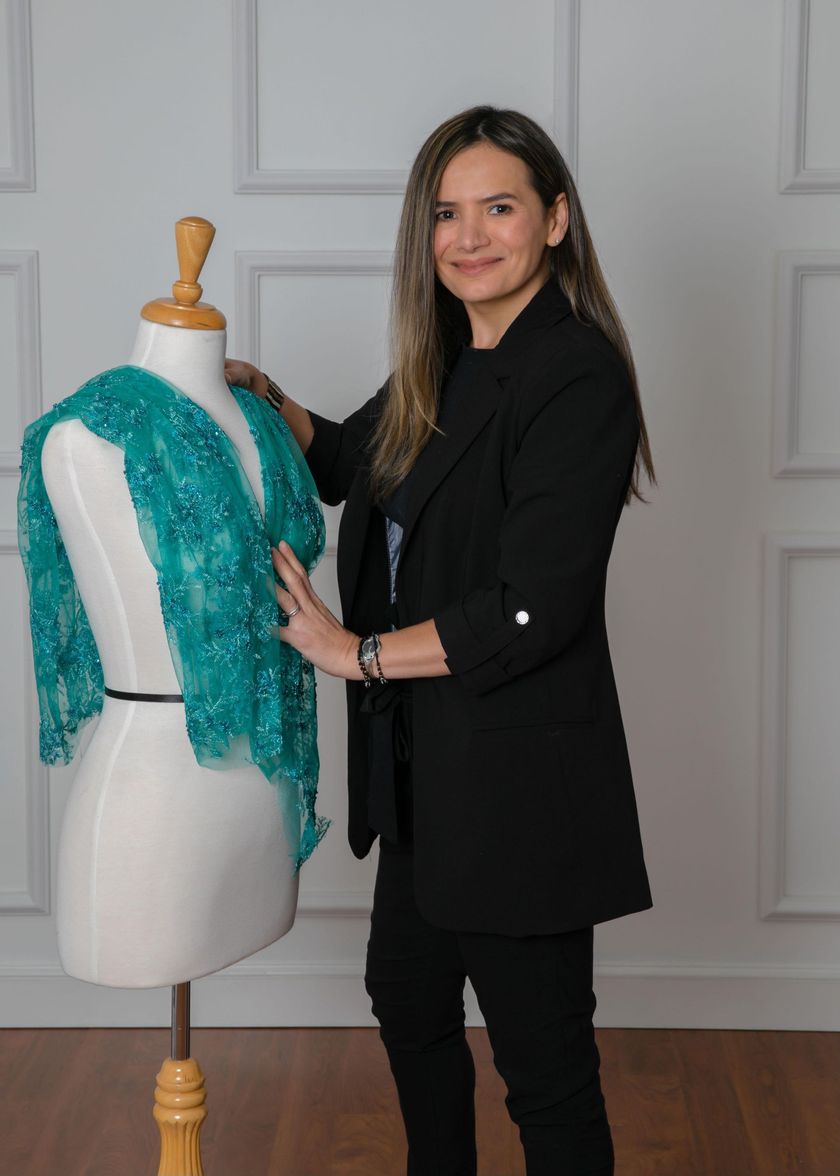 Woman in a black outfit standing beside a mannequin wearing a turquoise shawl in a studio.