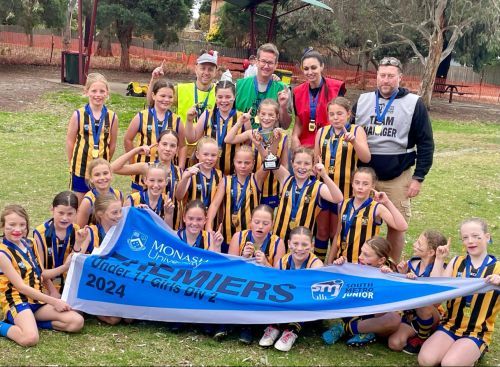 A group of youth athletes in yellow and black jerseys holding a 2024 premier championship banner with coaches behind them.