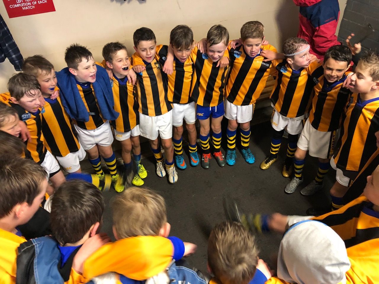 A group of teammates wearing black and yellow striped jerseys huddle together in a room.