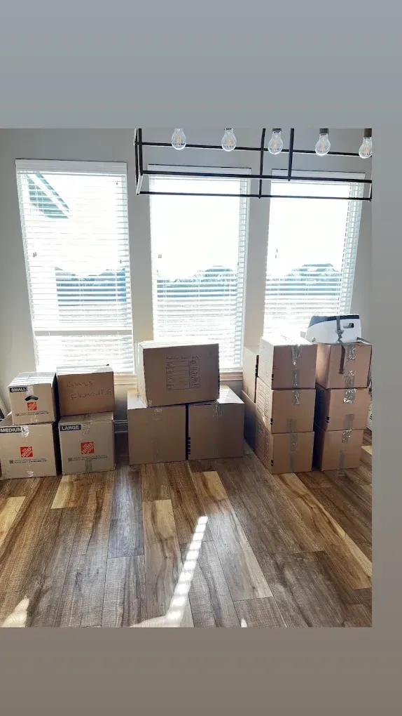 Boxes stacked on wooden floor in front of a window, indoors.
