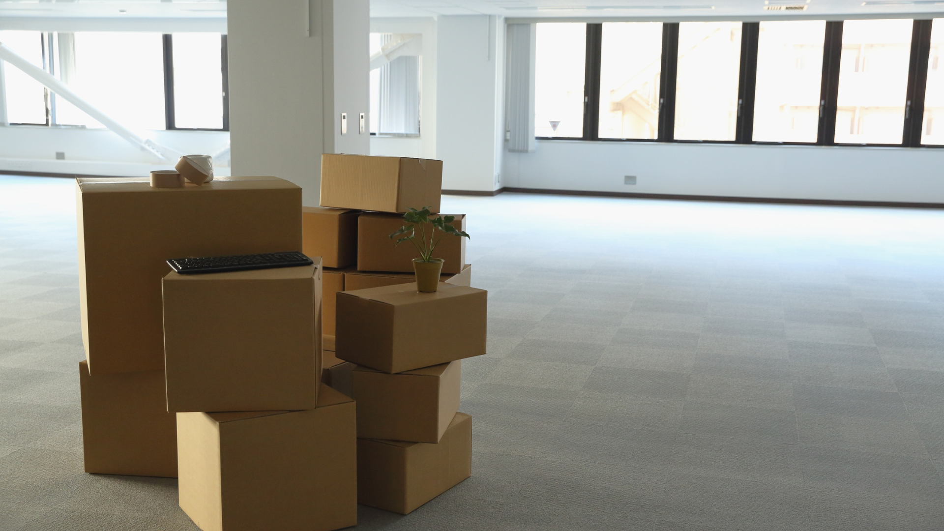 Cardboard boxes stacked in an empty, bright office space; moving boxes.
