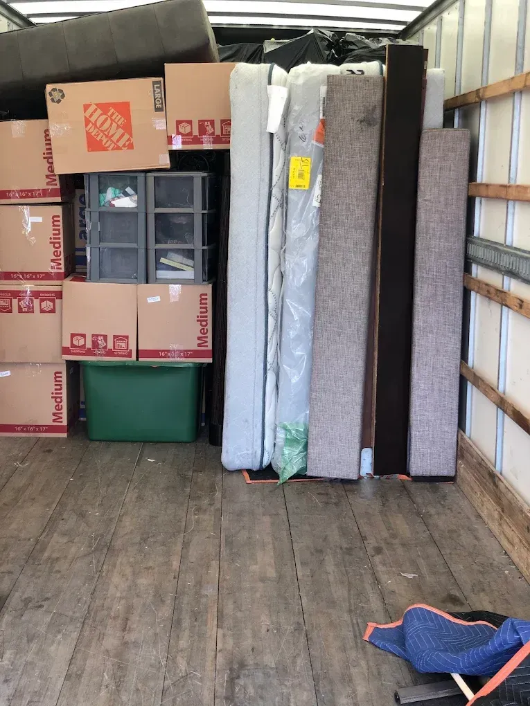 Moving truck filled with furniture, boxes, and a green bin. The floor is wooden.