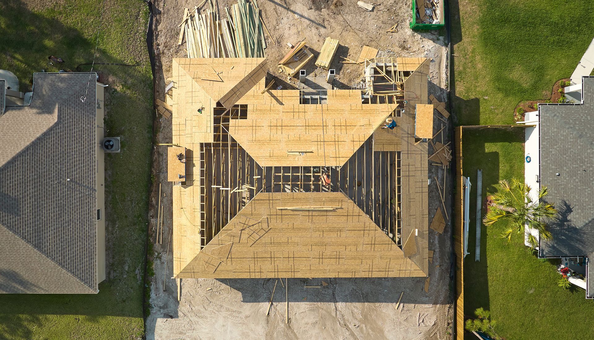 Overhead view of a house under construction; wood frame with partially laid roof.