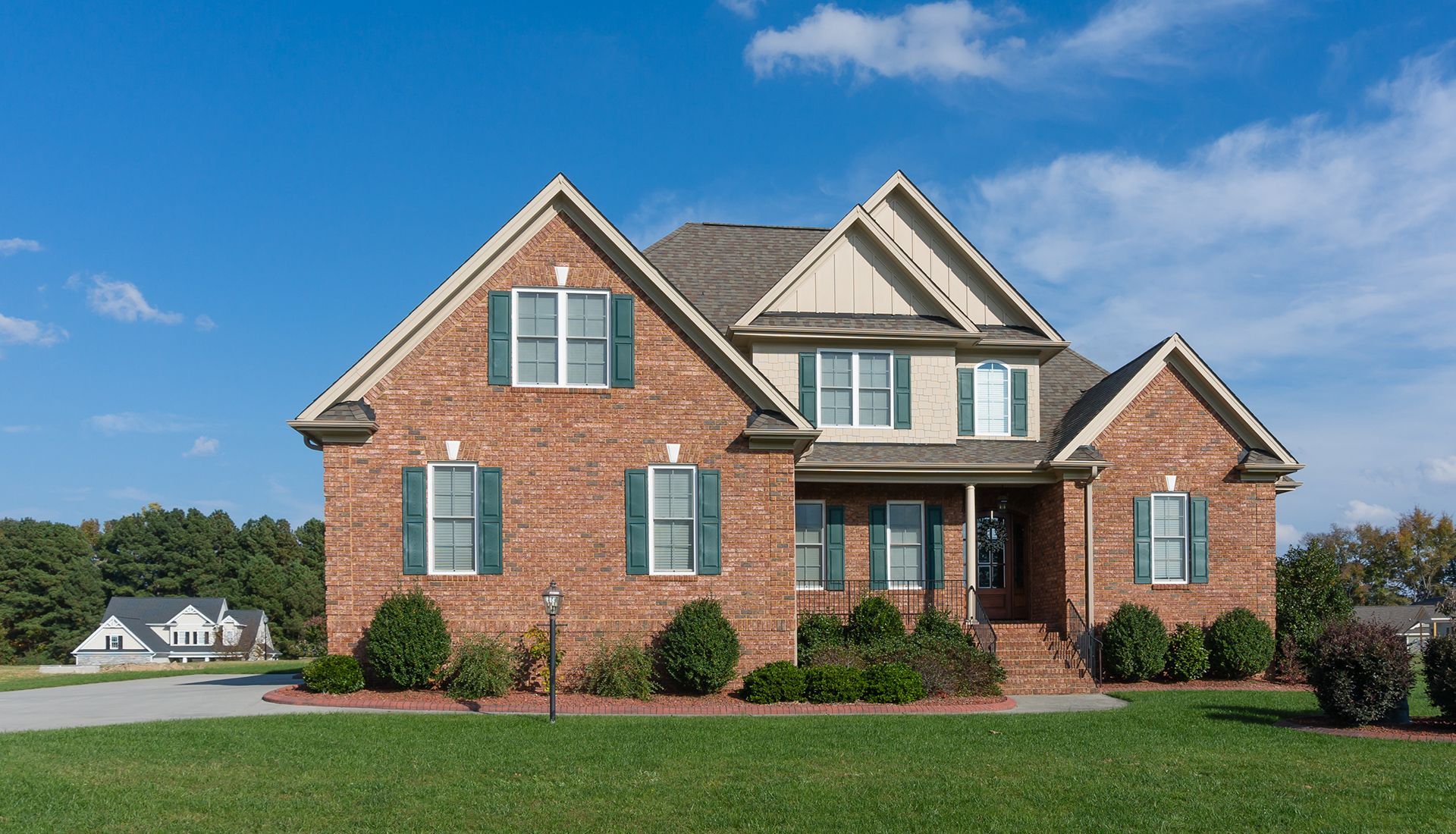 Brick house with green shutters, front lawn, and blue sky.