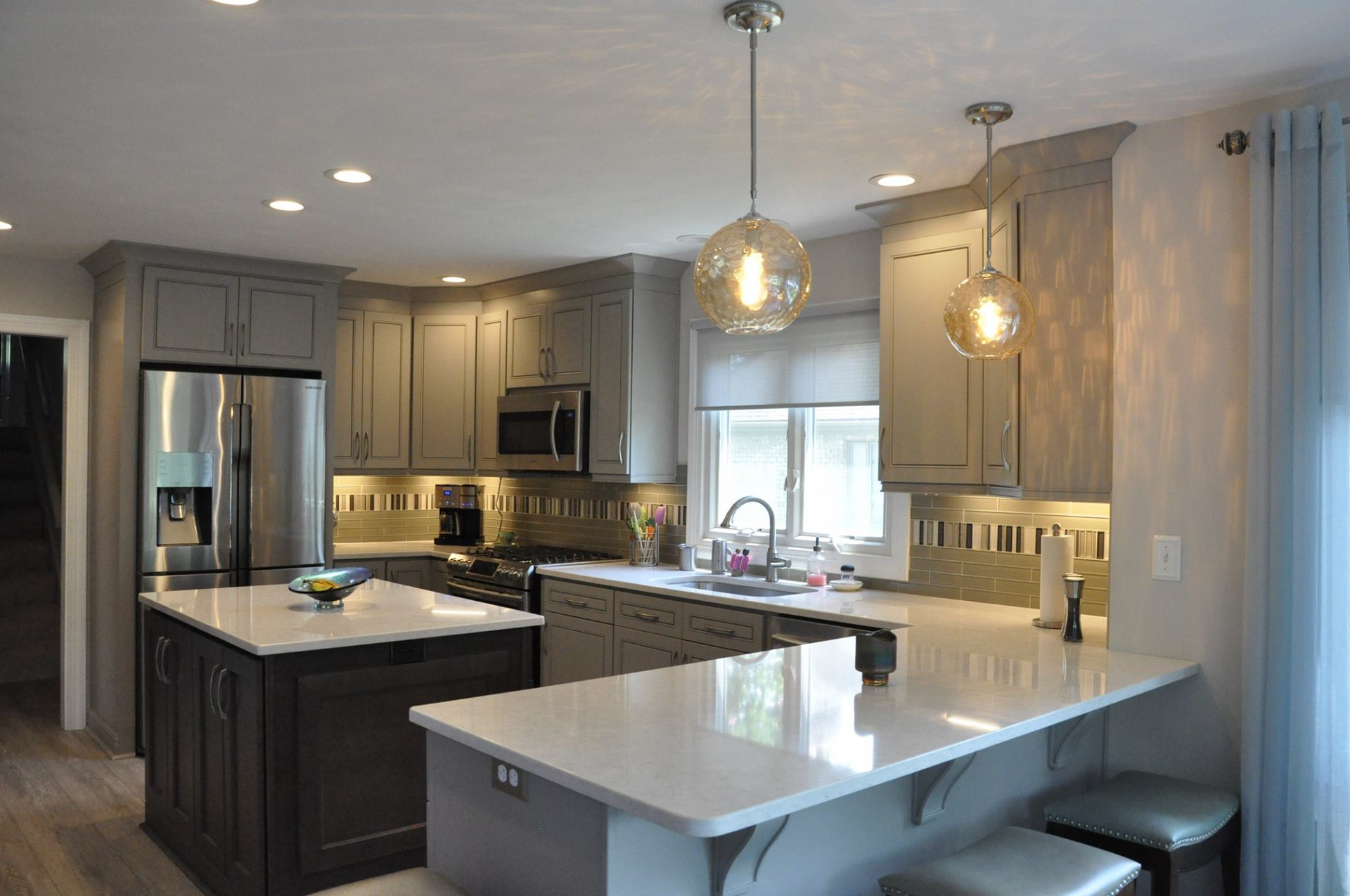 Modern gray kitchen with island, quartz countertops, and globe pendant lights.