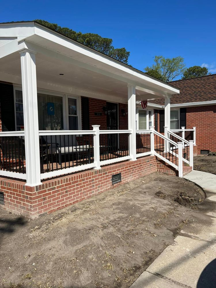 Red brick house with white porch, railing, and columns under a bright blue sky.