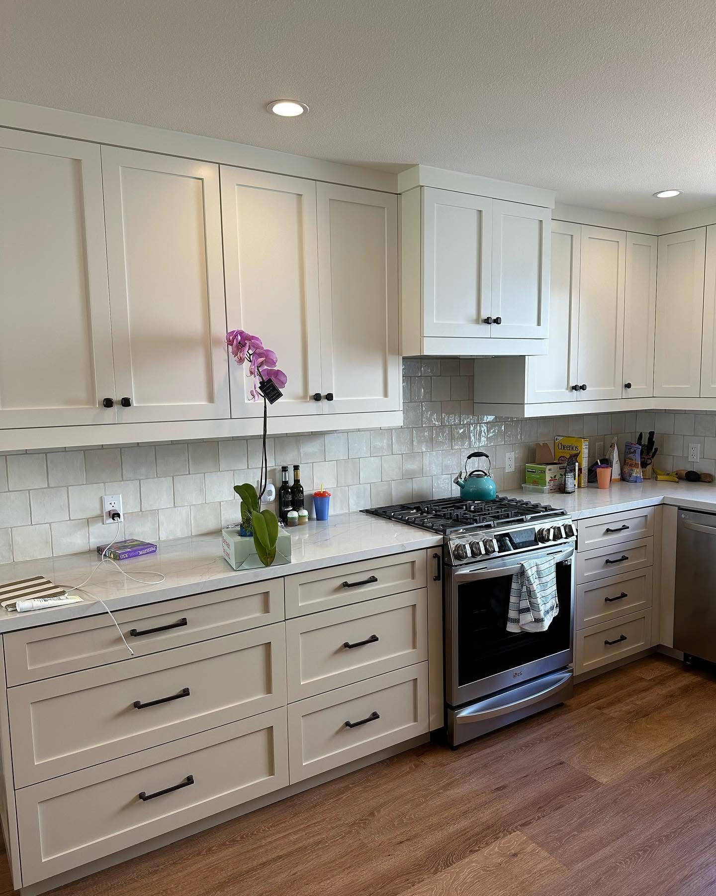 Bright kitchen with white cabinets, gray counters, stainless stove, and a purple orchid on the island.