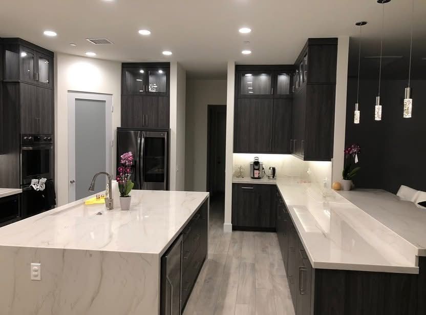 Modern kitchen with dark cabinets, white islands, pendant lights, and stainless steel appliances
