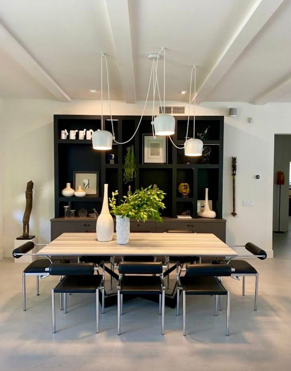 Modern dining room with long wooden table, black chairs, pendant lights, and built-in shelving