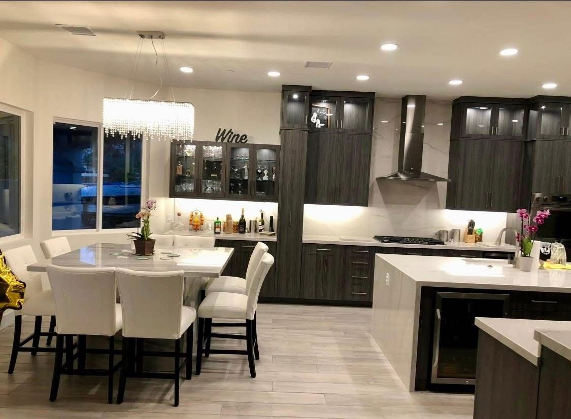 Modern kitchen and dining area with white chairs, dark cabinets, and a large island under warm lighting