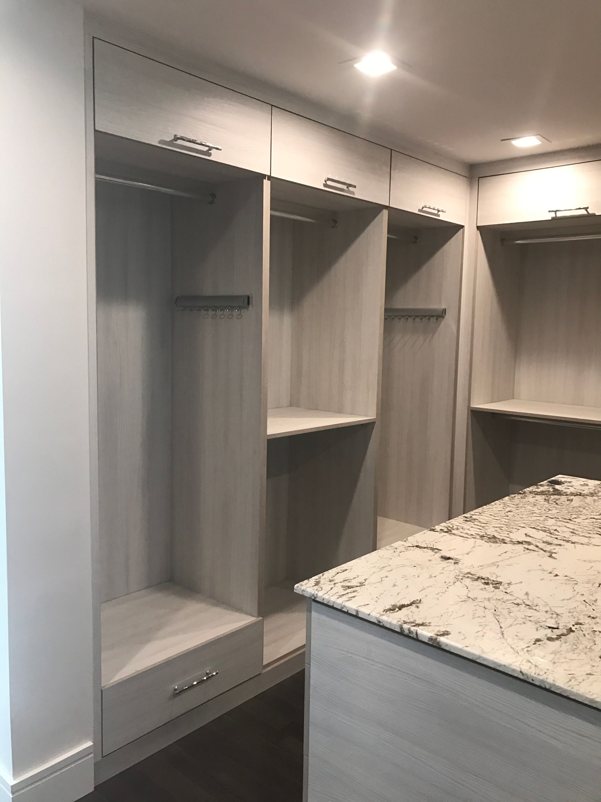 Walk-in closet with built-in gray shelves, hanging rods, and a marble-top island under recessed lights