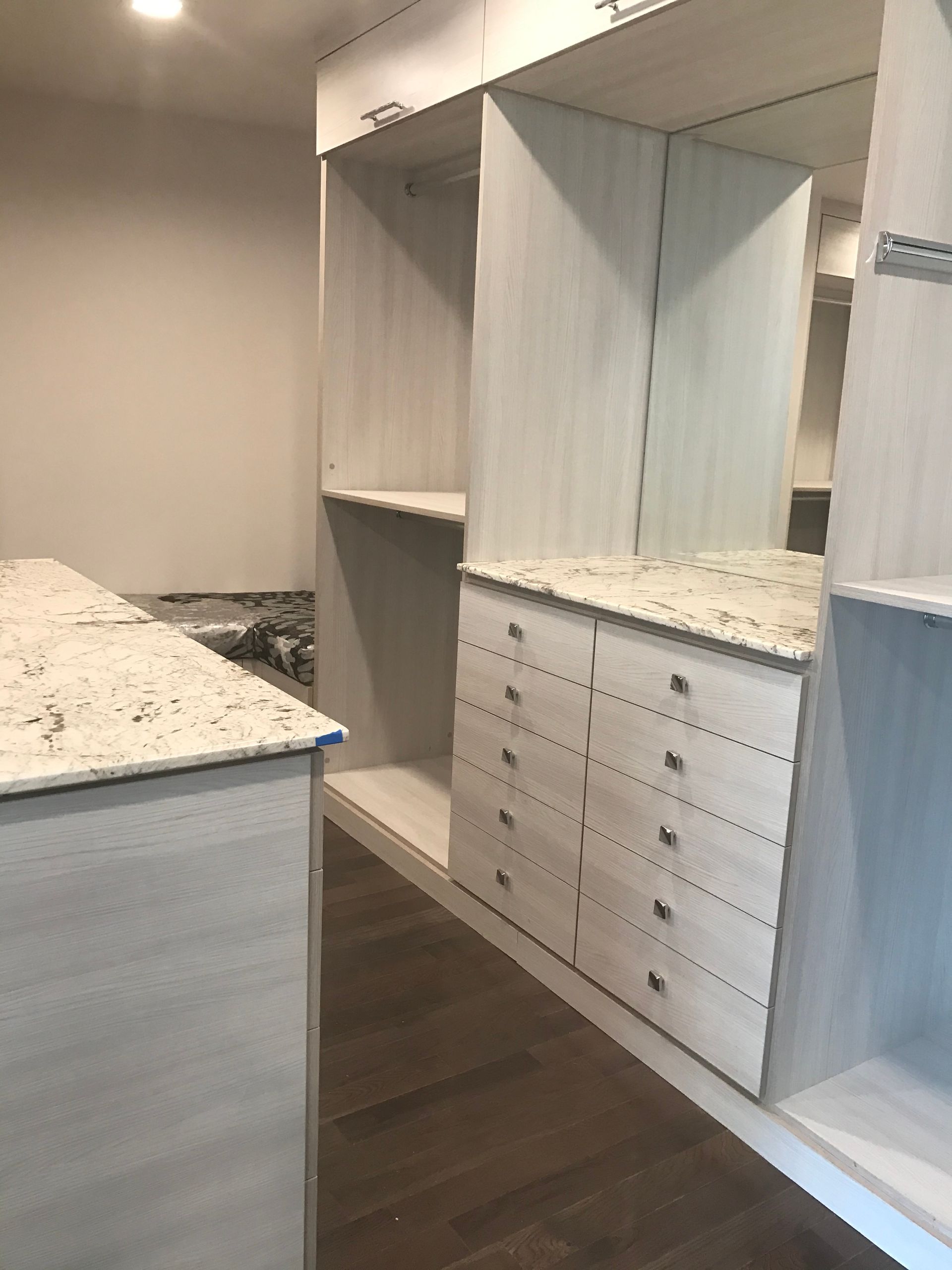 Built-in white closet shelving and drawers in a bright bedroom with dark wood floors.