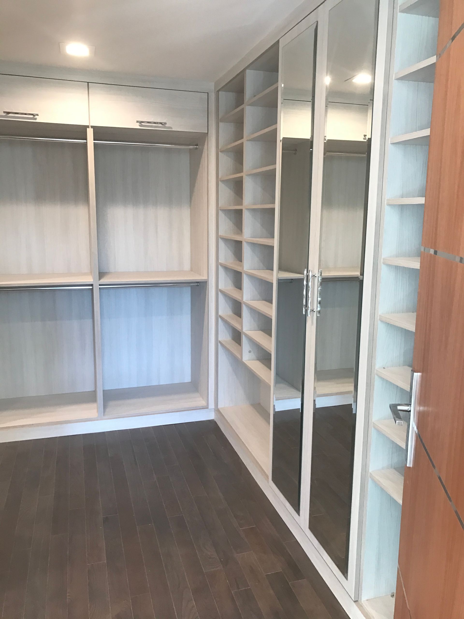 Empty walk-in closet with white shelving, mirrored doors, wood floor, and open hanging space.