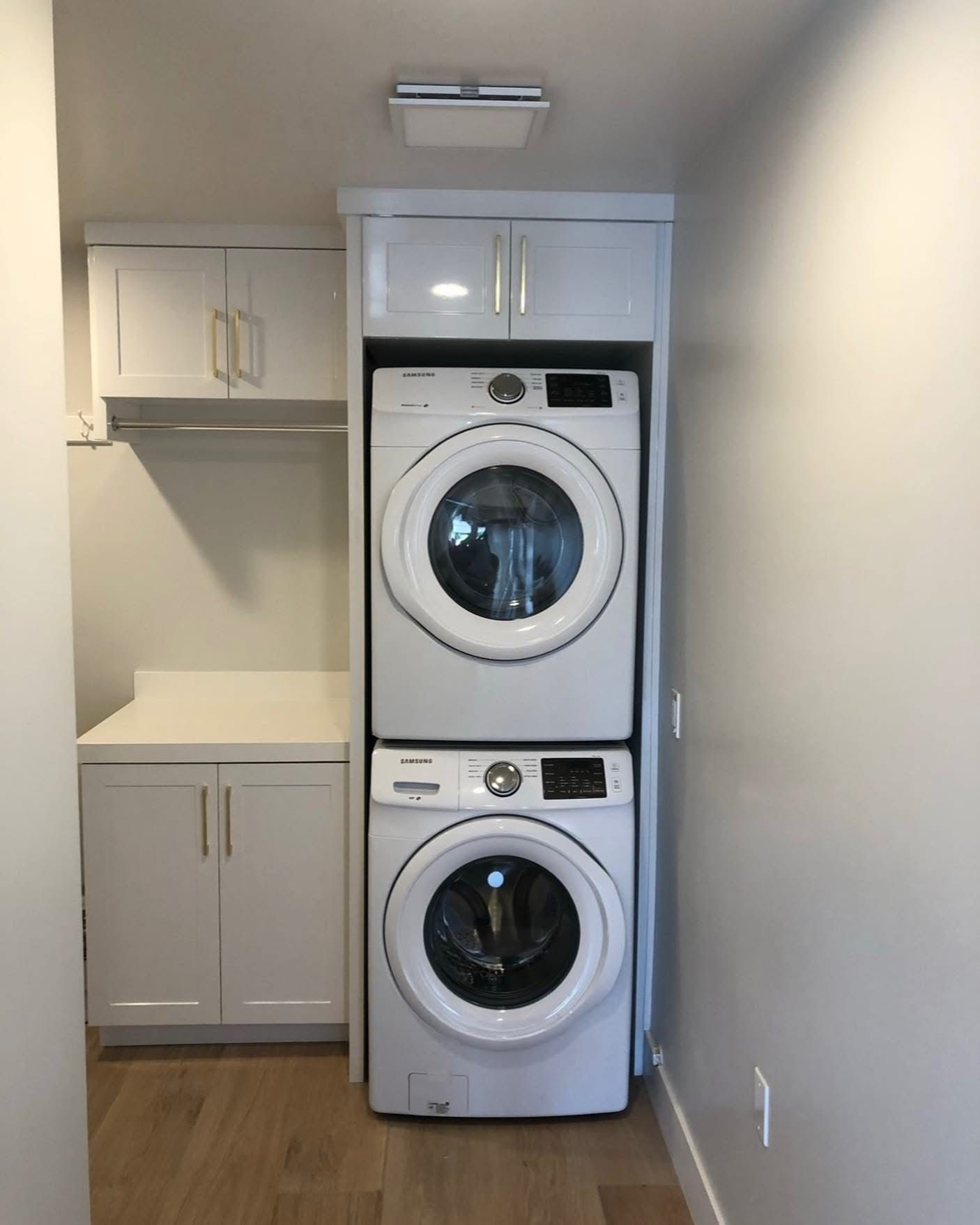 Laundry closet with stacked white washer and dryer, cabinets, and wood floor