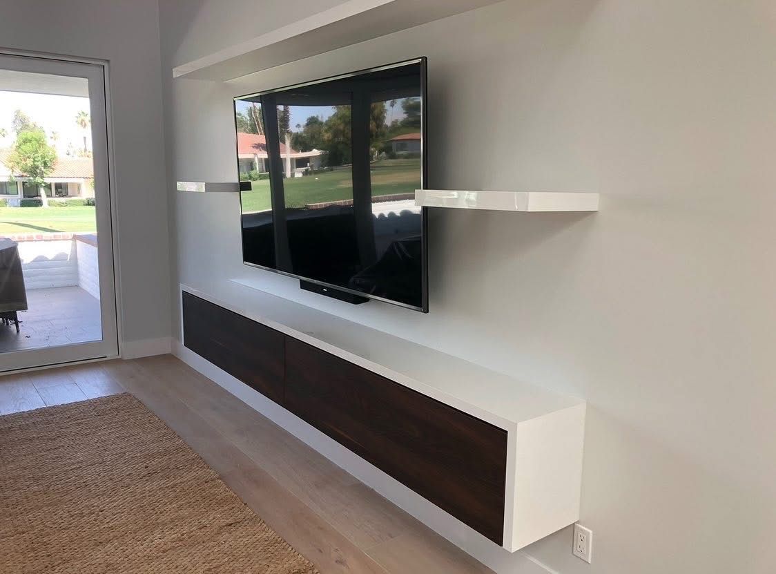 Modern living room with wall-mounted TV, floating shelves, and a long dark cabinet under it.