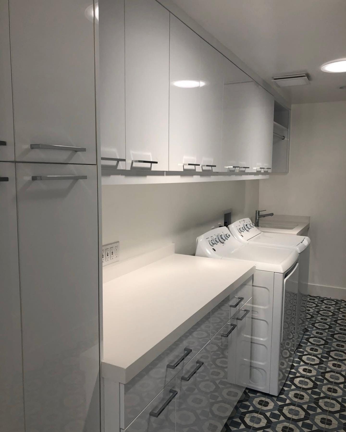 Bright laundry room with white cabinets, countertop, washer and dryer, and patterned tile floor.