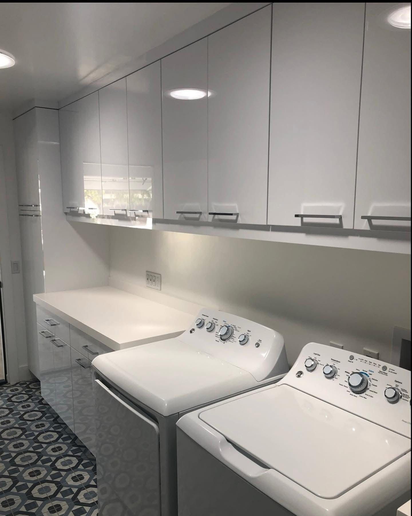 Modern laundry room with white cabinets, countertop, and a washer and dryer in front of patterned tile flooring.