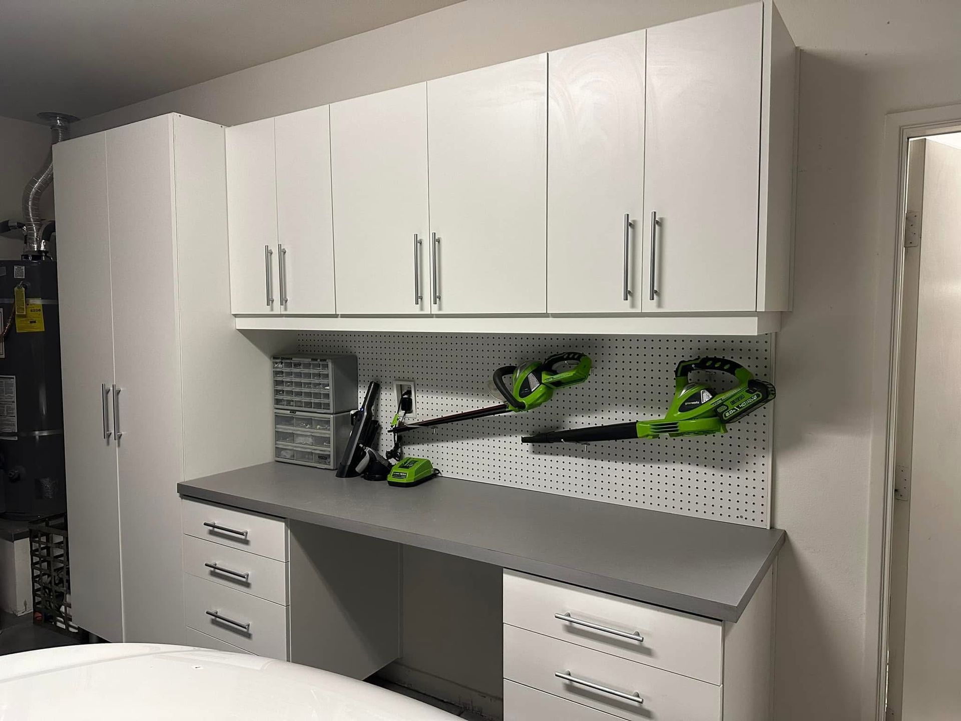 White garage cabinets and workbench with green power tools on a pegboard wall.