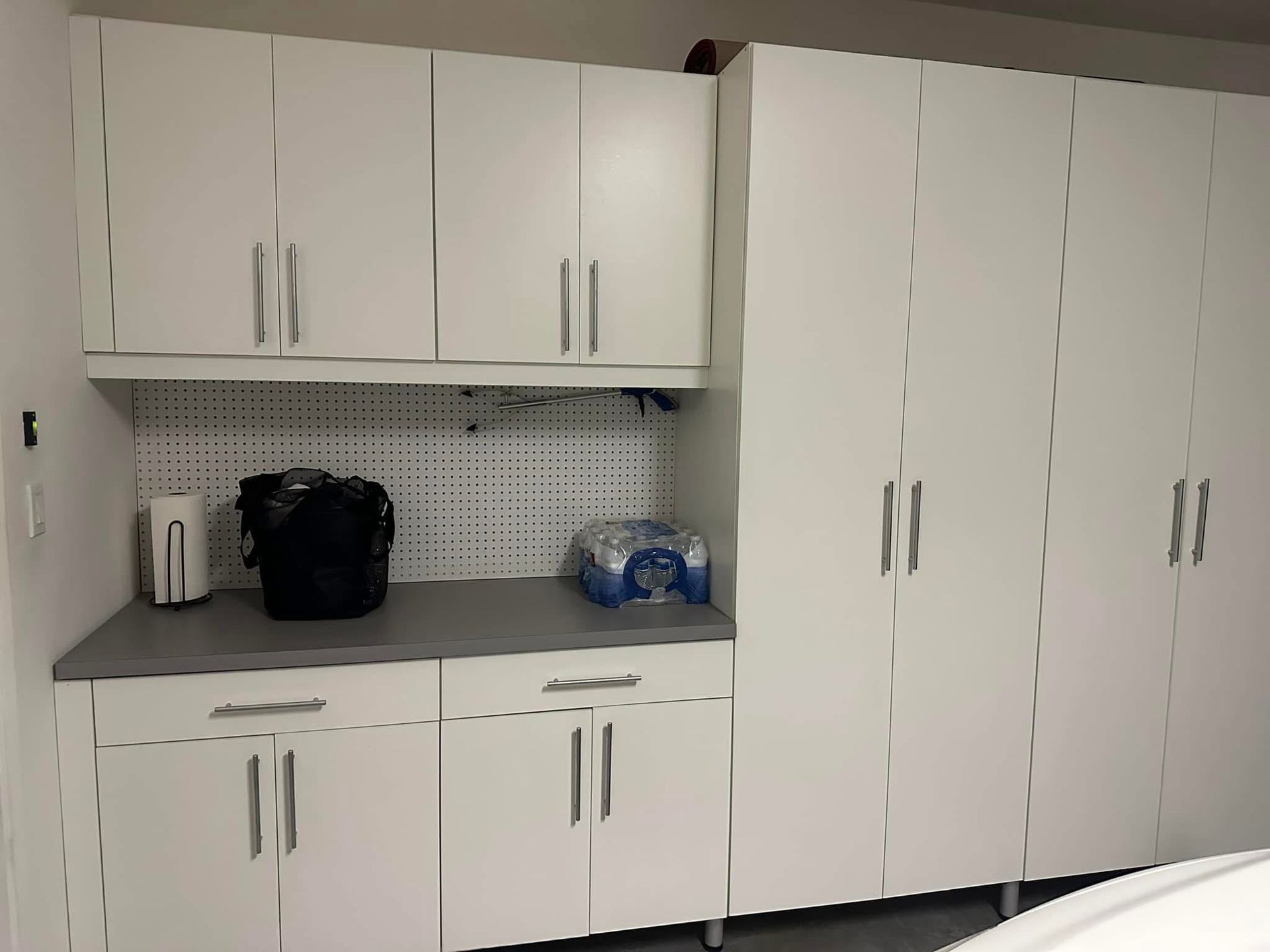 White office kitchenette with cabinets, countertop, sink, and a pack of bottled water on the right
