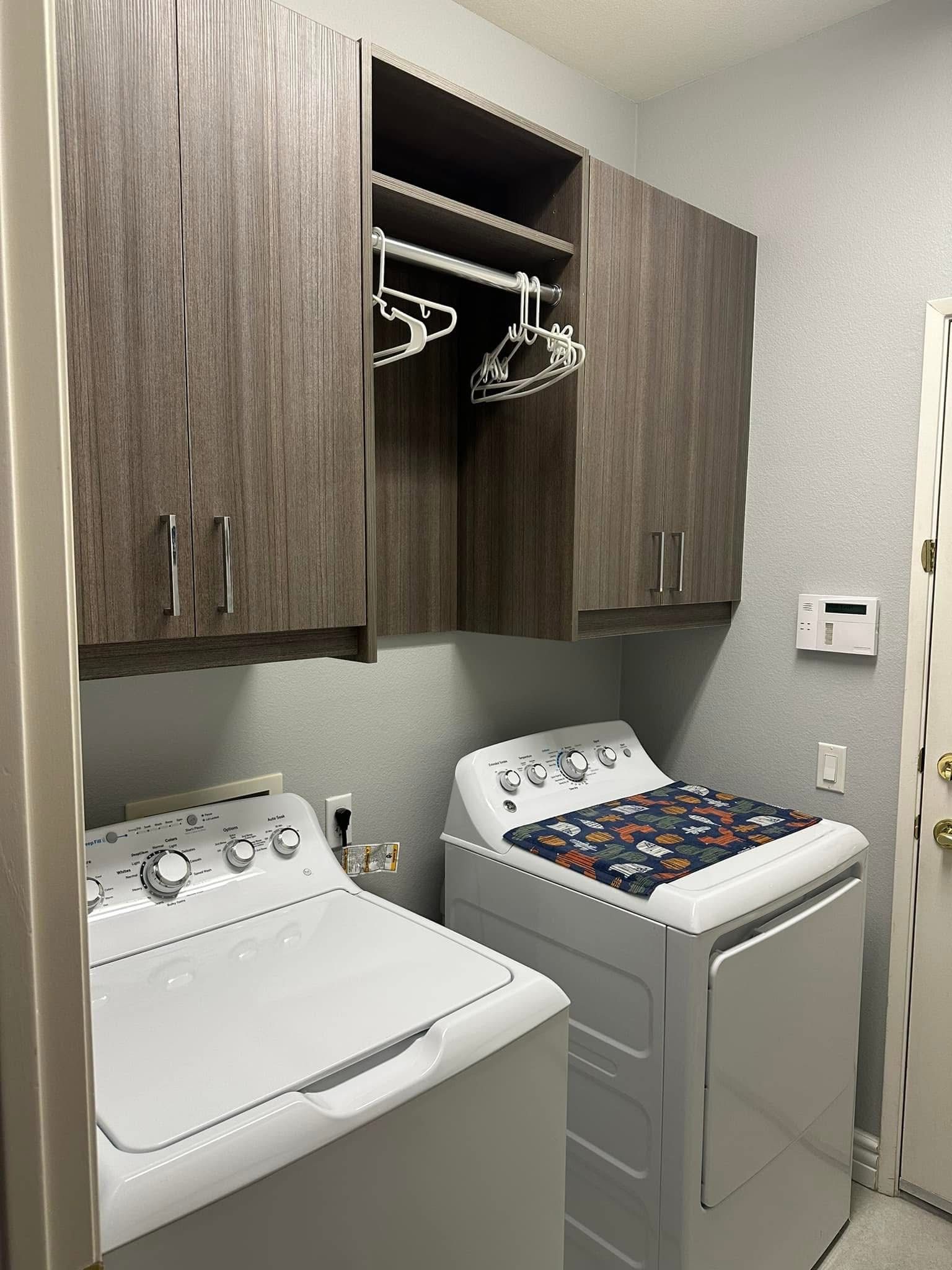 Laundry room with washer and dryer under wood cabinets and hanging clothes rods