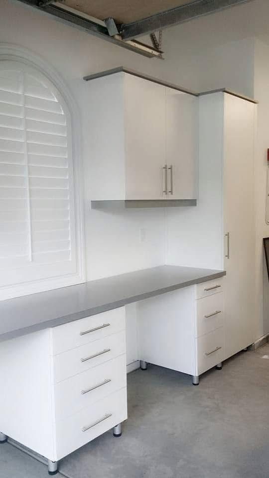 White garage workbench with cabinets, gray countertop, pegboard, and green tools mounted on the wall