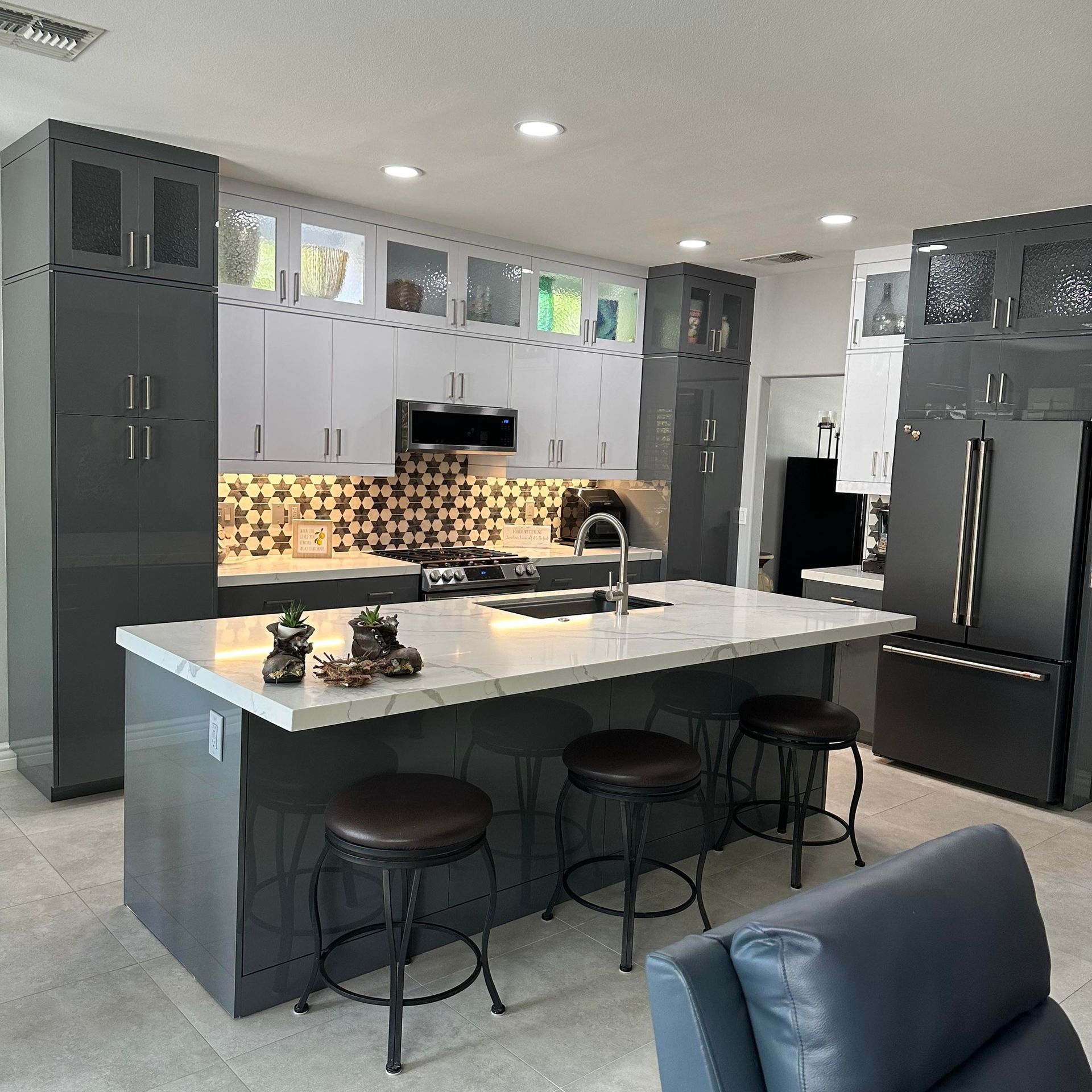 Modern gray kitchen with a large island, bar stools, pendant lights, and black appliances
