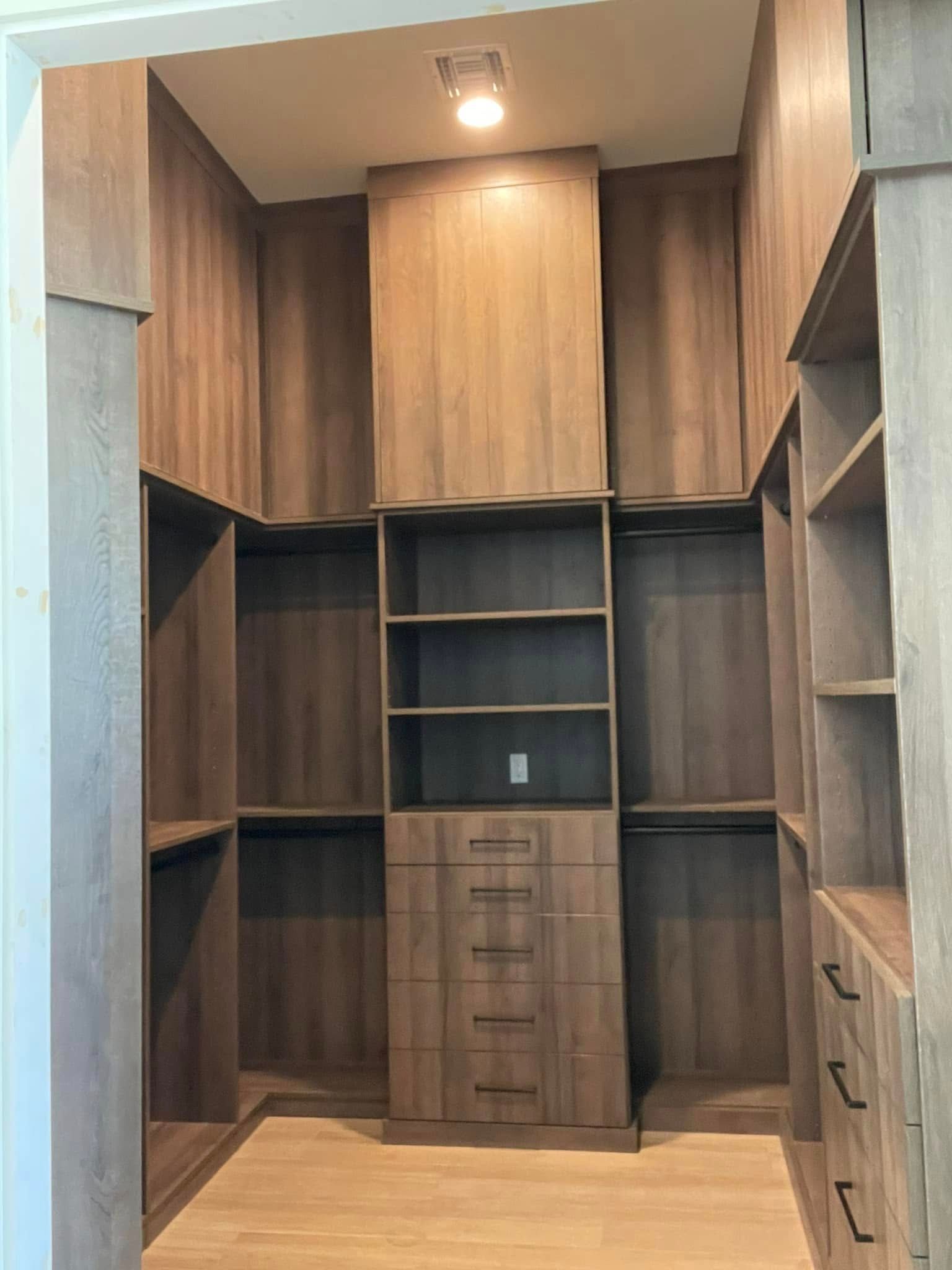 Walk-in closet with wood-paneled built-ins, shelves, drawers, and a ceiling light.