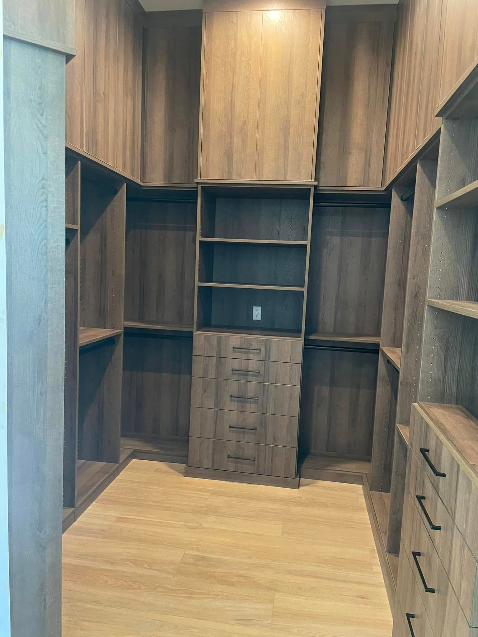 Walk-in closet with dark wood shelving, cabinets, and drawers on both sides and at the back