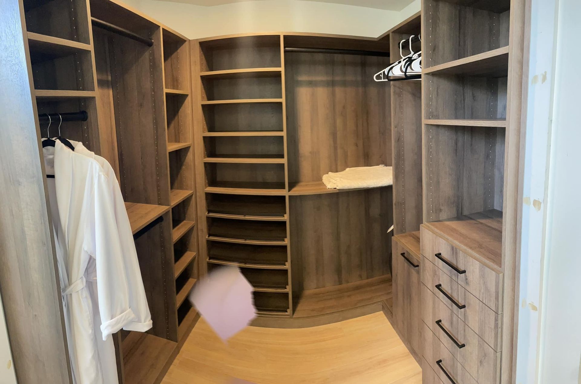 Walk-in closet with wood shelves, hanging clothes, drawers, and a pink item on the floor.