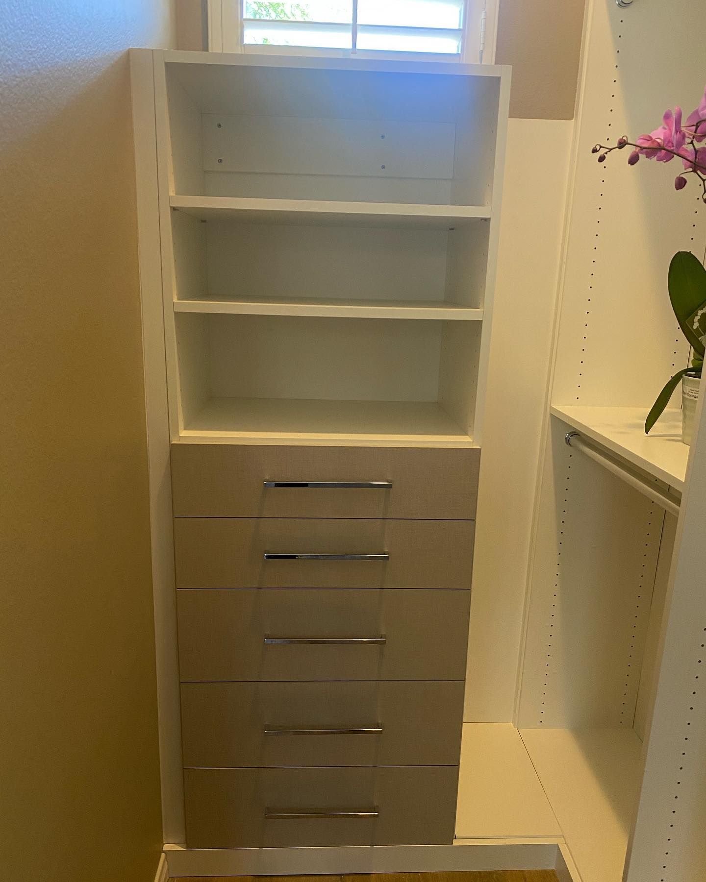 White shelving unit with open shelves and small drawers in a bright room near a window.