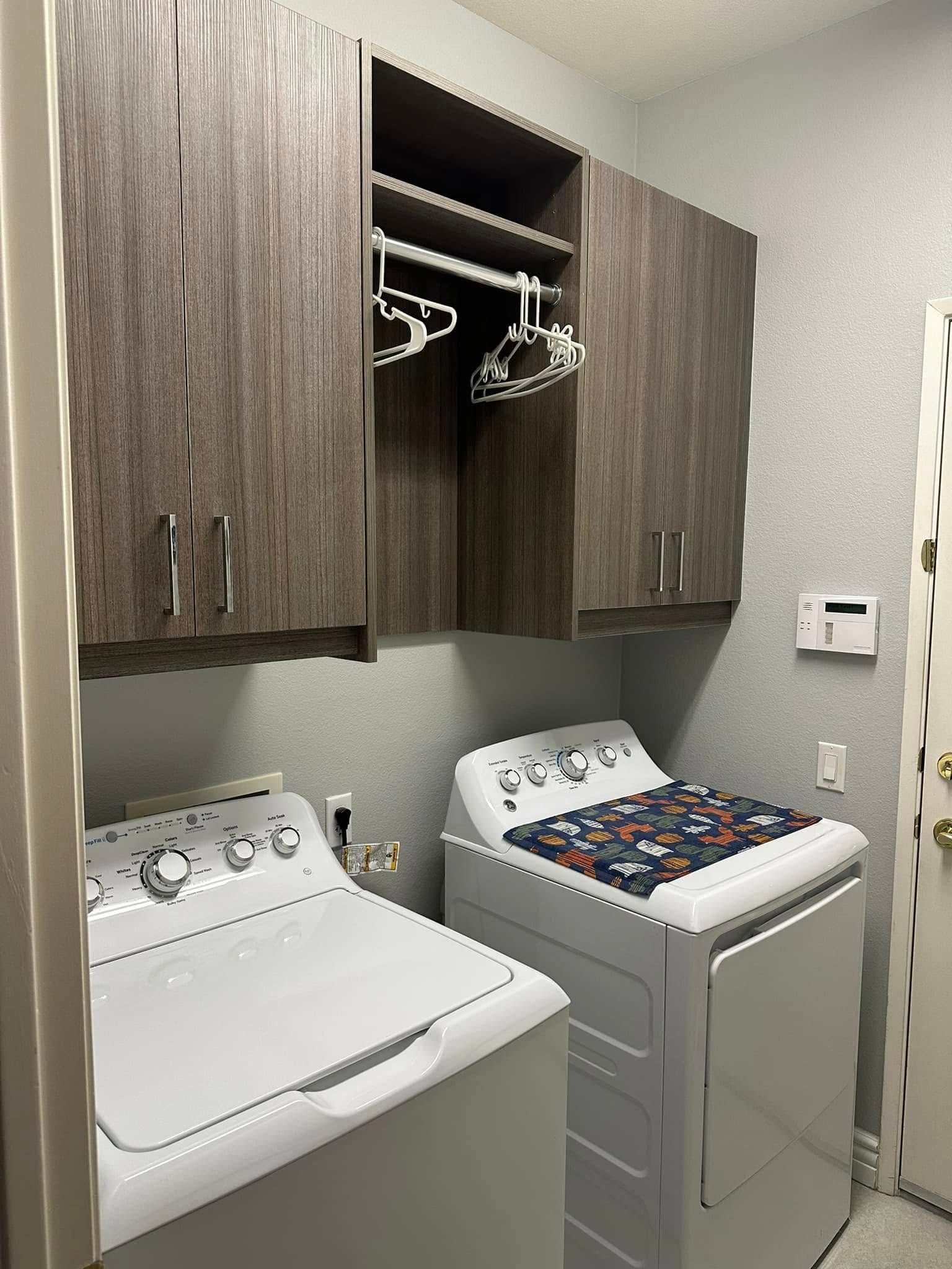 Laundry room with white washer and dryer beneath wood cabinets and hanging closet rods
