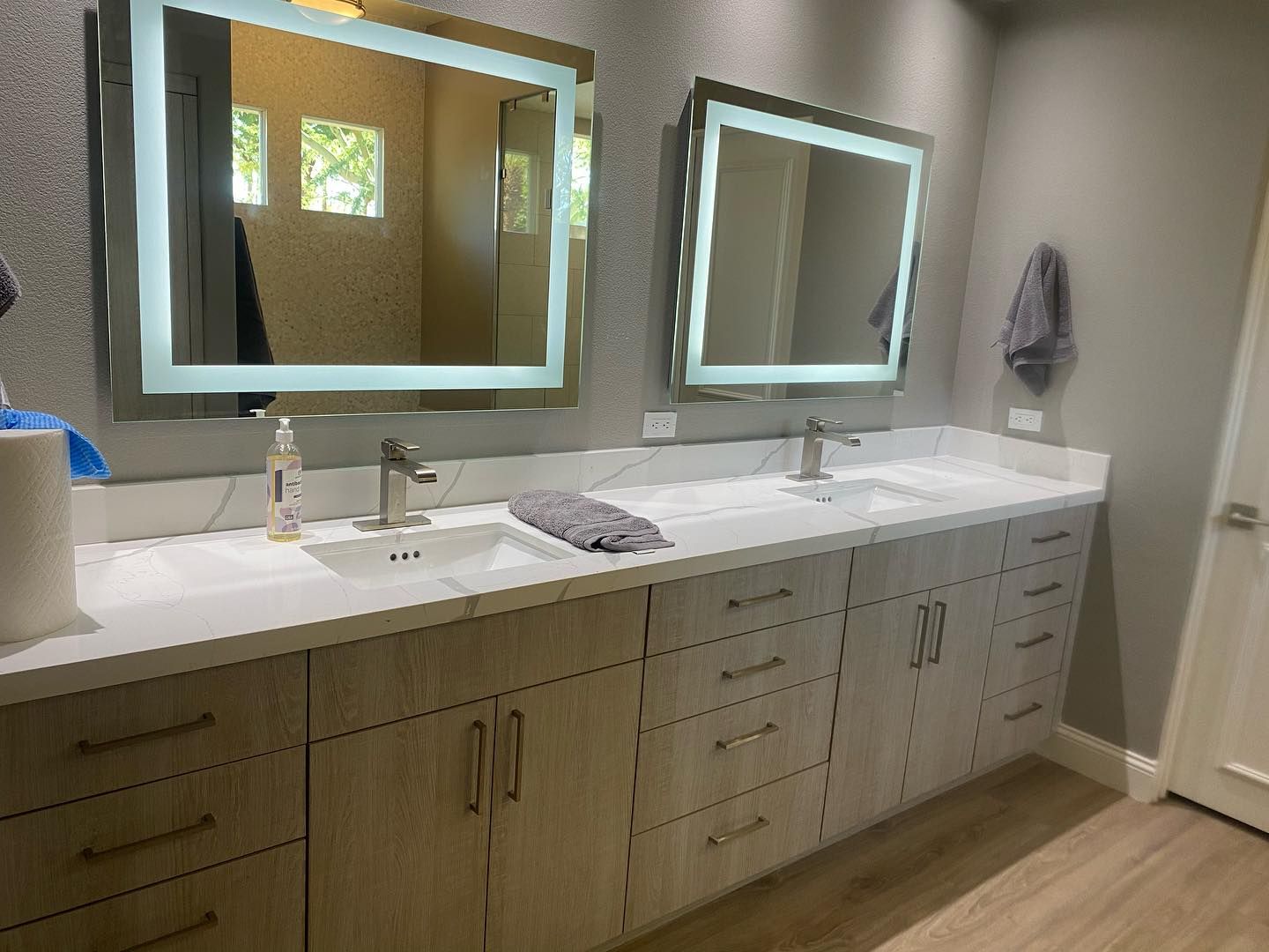 Modern bathroom with double sinks, lit mirrors, and wood cabinets