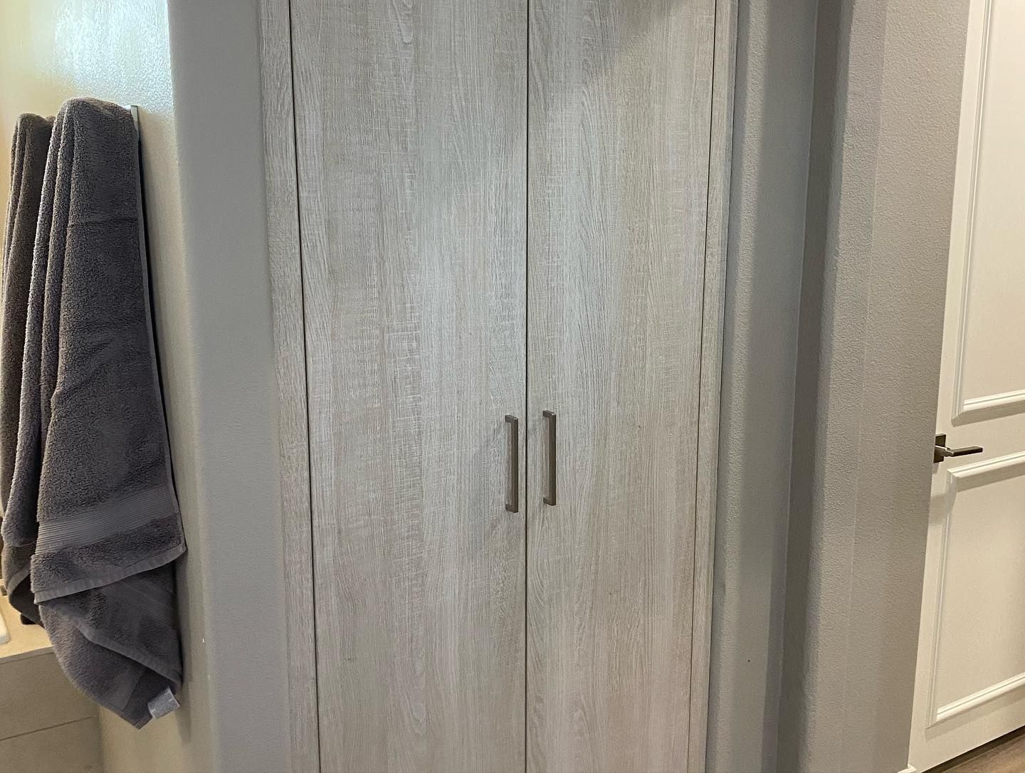 Gray bathroom cabinet beside a towel rack and partially open white door