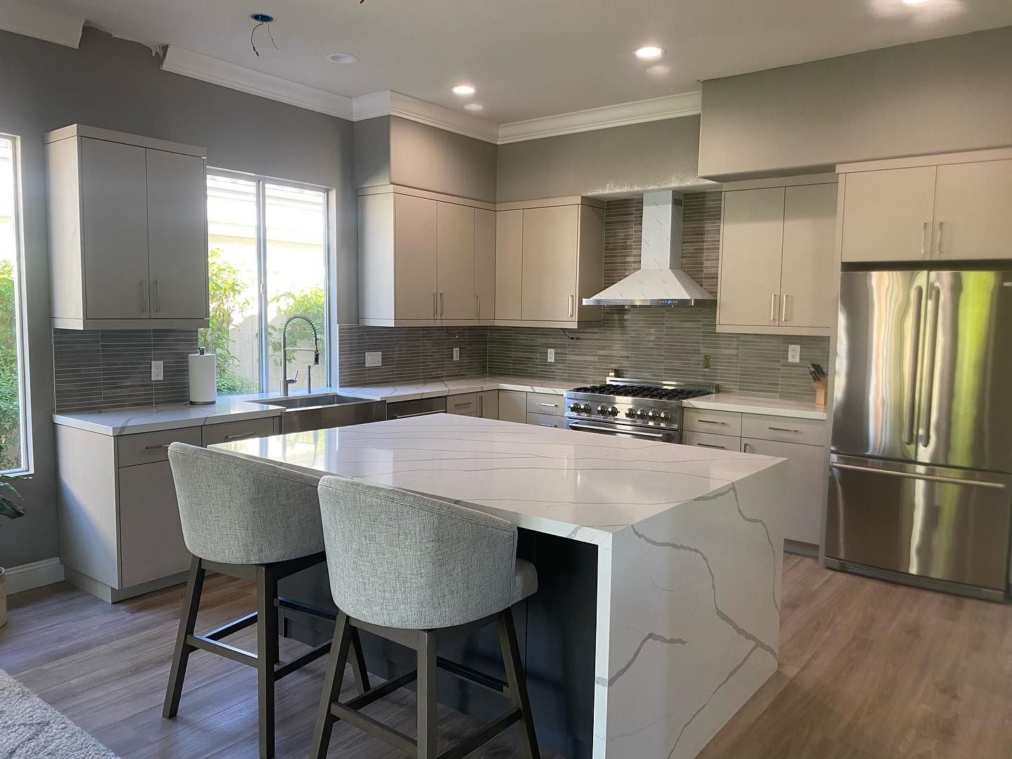 Modern kitchen with white island, gray cabinets, stainless steel appliances, and two upholstered stools