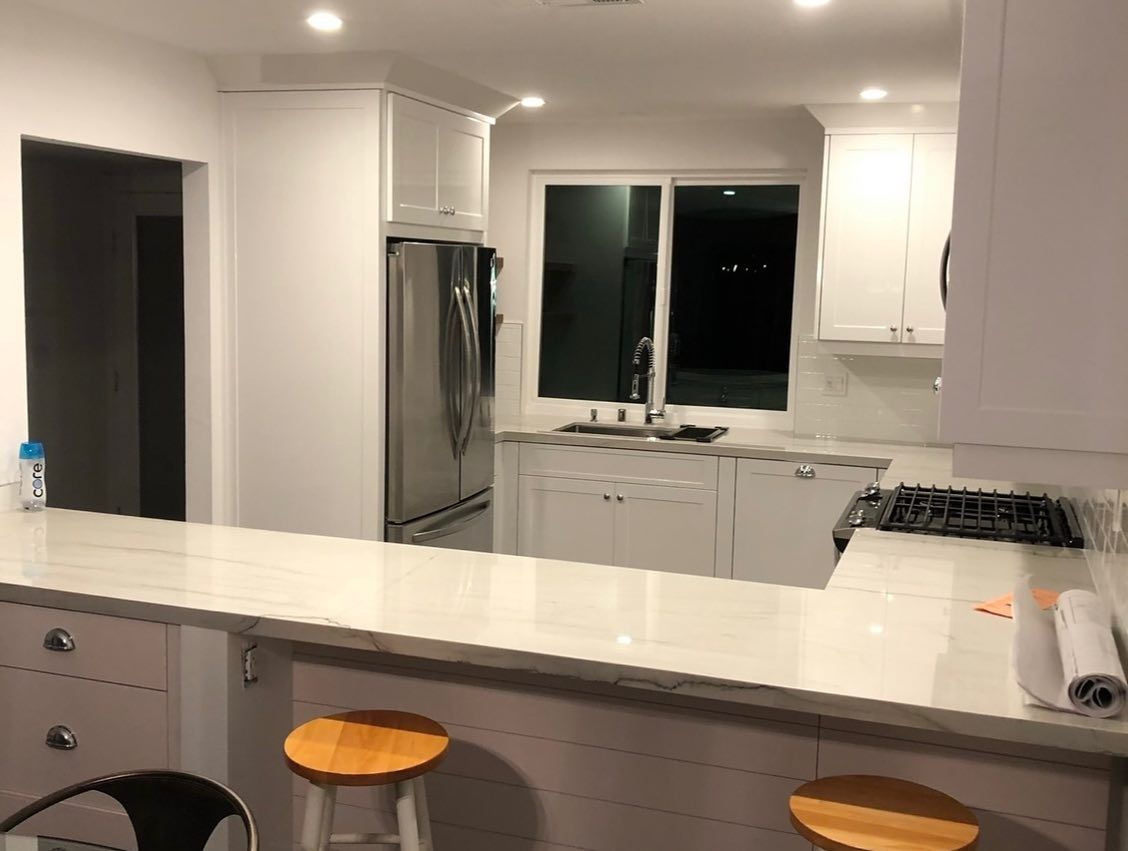 Modern white kitchen with island, stainless steel fridge, sink under window, and two orange stools