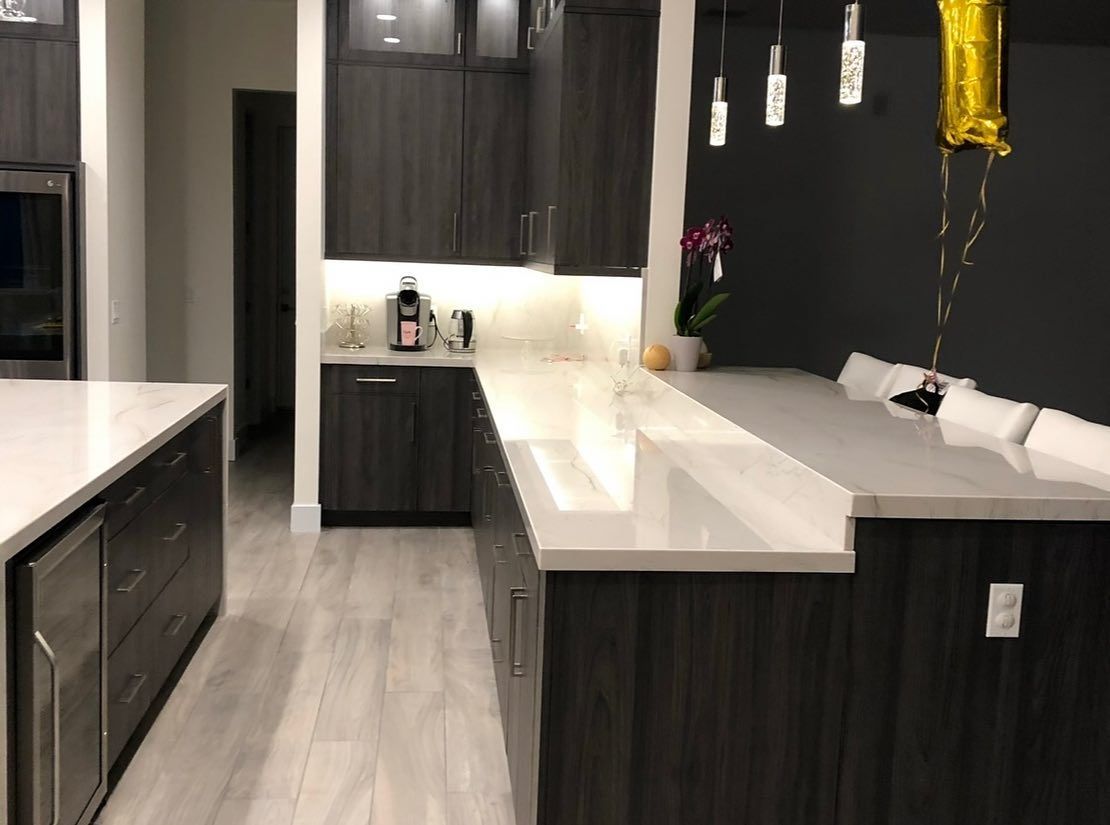 Modern kitchen with dark cabinets, white countertops, and a central island under pendant lights