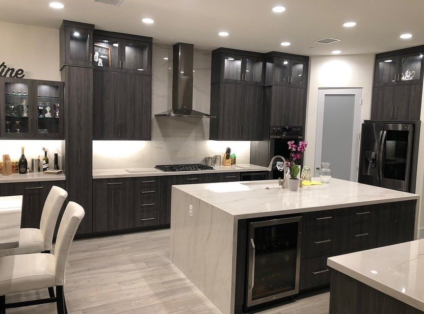 Modern kitchen with dark cabinets, white island, stainless steel appliances, and recessed ceiling lights