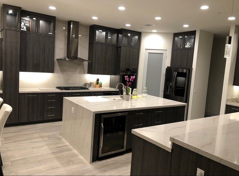 Modern kitchen with dark cabinets, white island, stainless appliances, and recessed ceiling lights