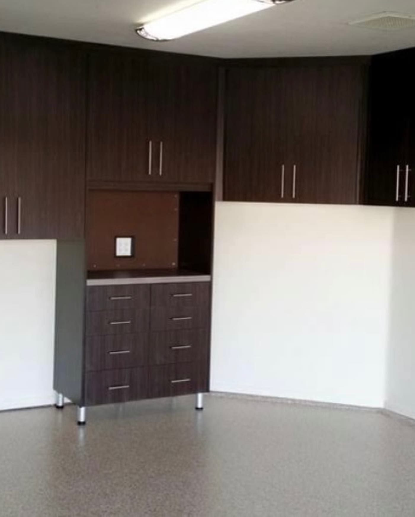 Empty room with dark wood cabinets, white wall panels, and gray floor tiles