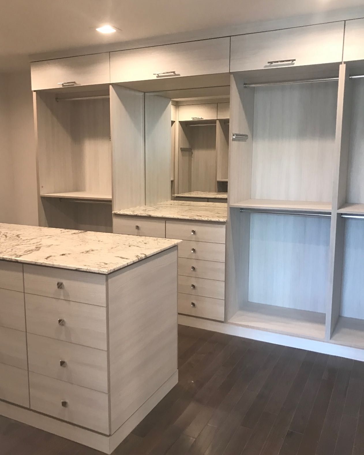 Empty walk-in closet with light wood built-ins, white shelves, and a speckled island with drawers