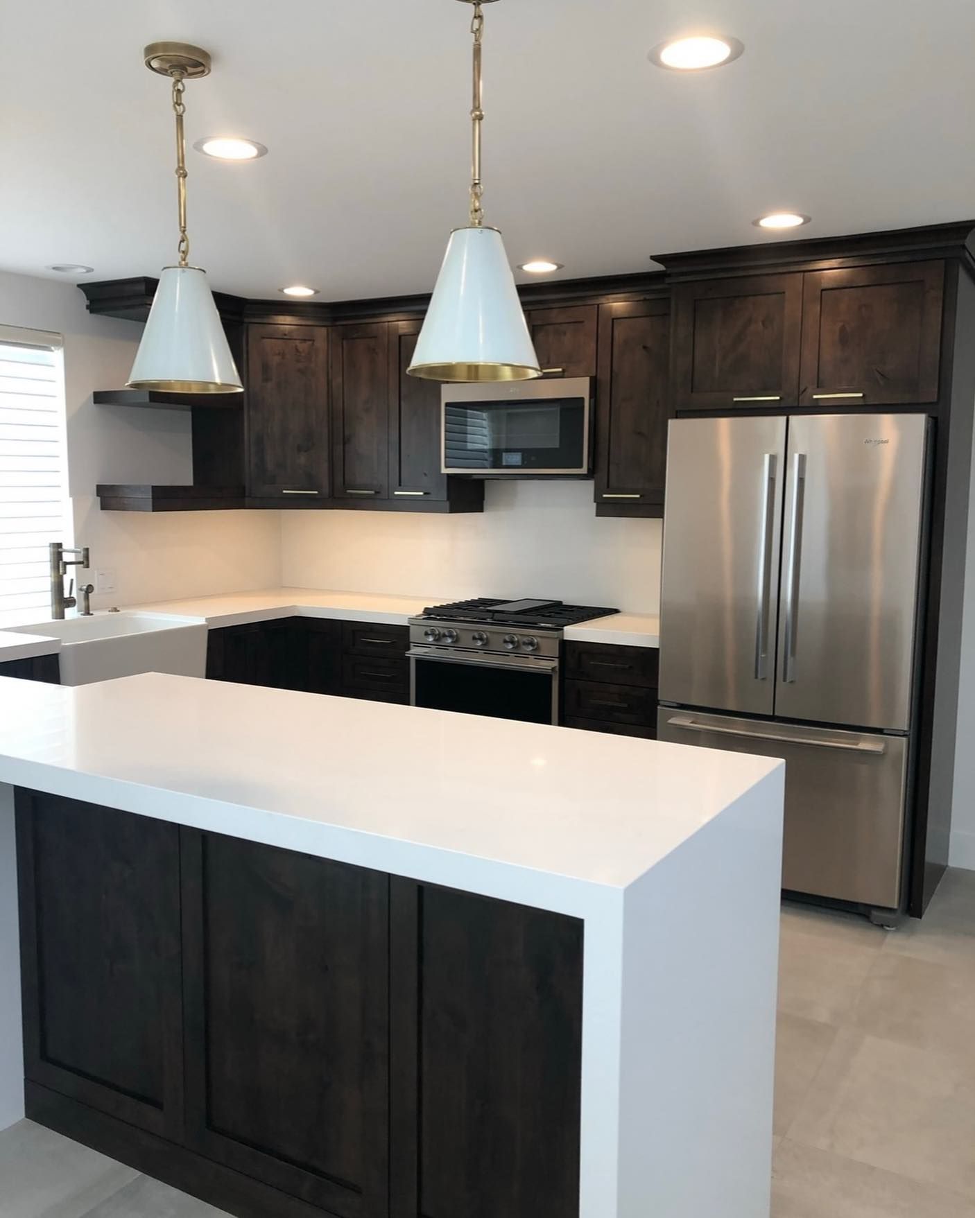 Modern kitchen with dark wood cabinets, stainless steel appliances, and white island countertops