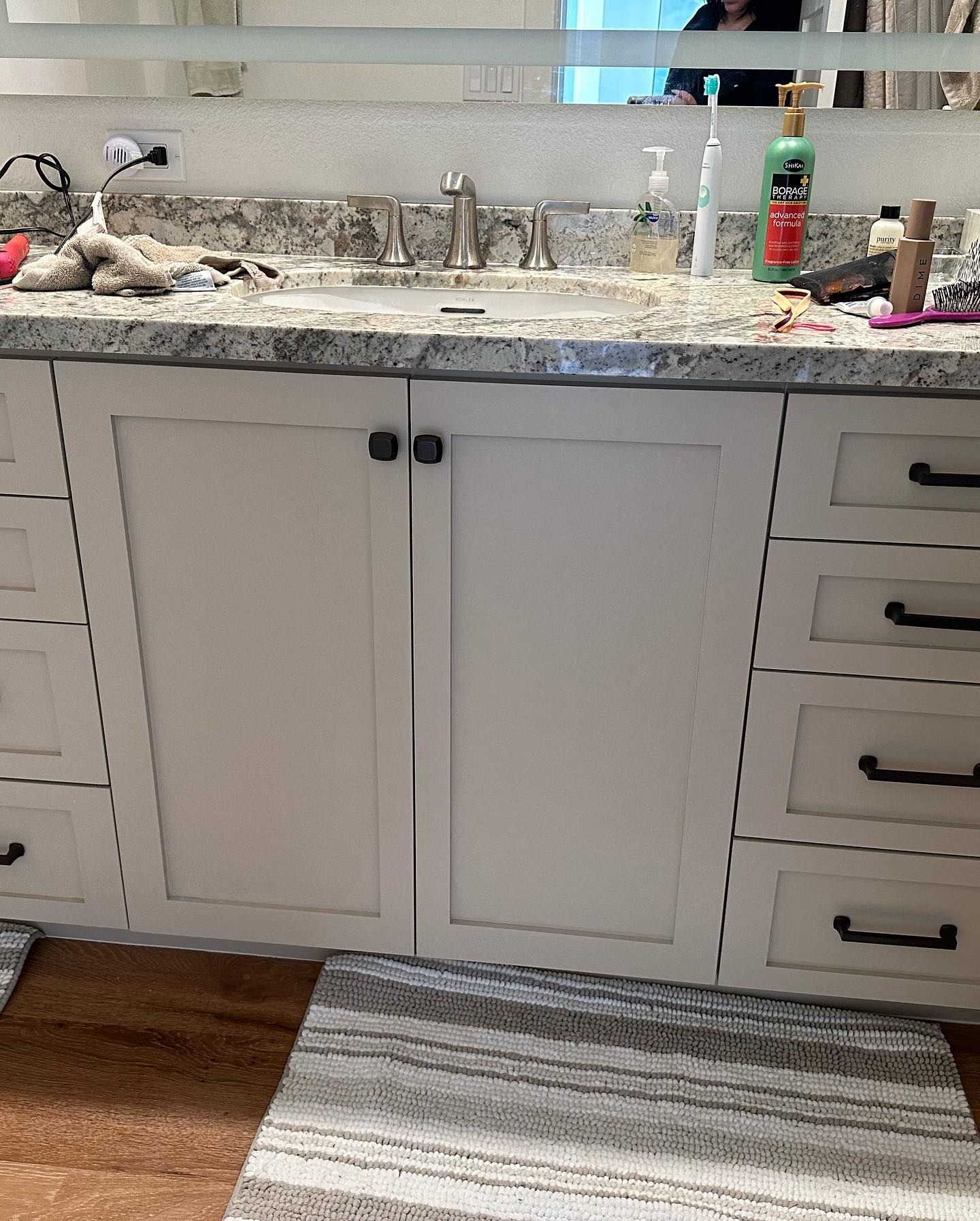 Bathroom vanity with white cabinets, granite countertop, sink, and toiletries on top.
