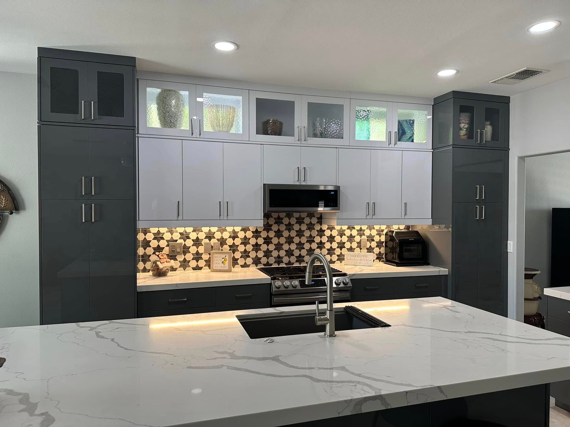 Modern kitchen with white island, gray cabinets, mosaic backsplash, and stainless range hood