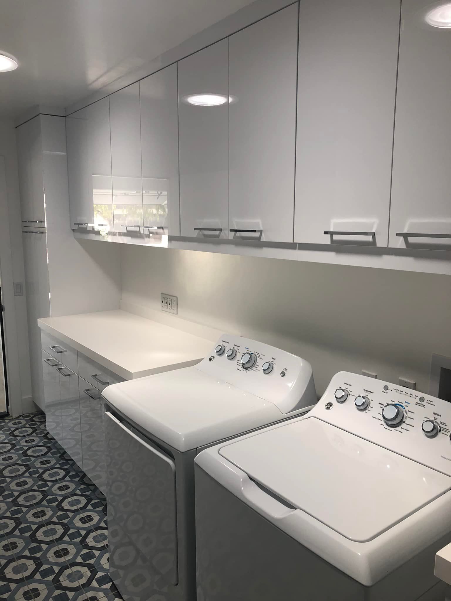 Laundry room with white cabinets, counter, and two washers and dryers on a patterned floor.