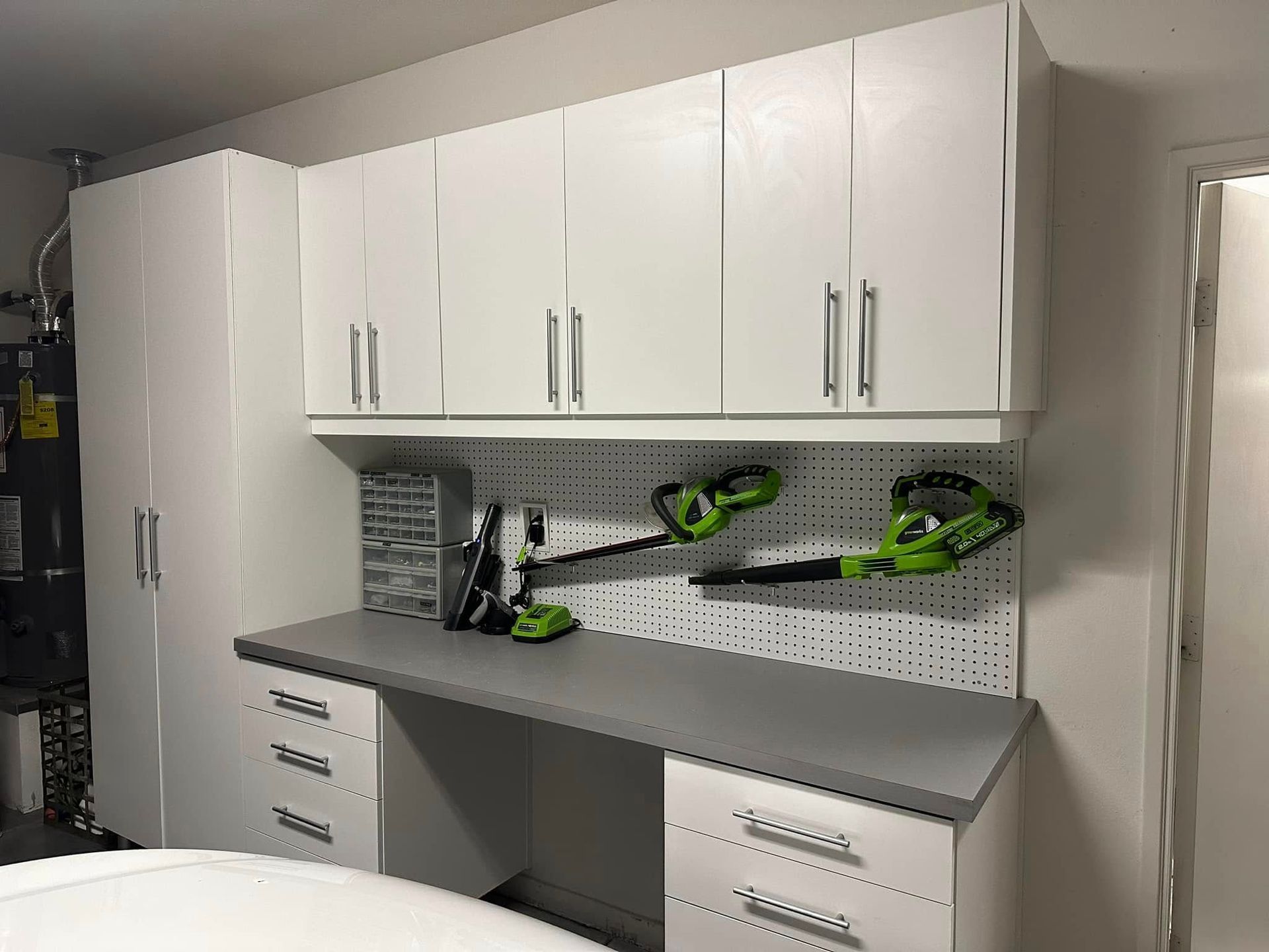 White garage cabinets and workbench with green power tools on a gray countertop and pegboard back wall