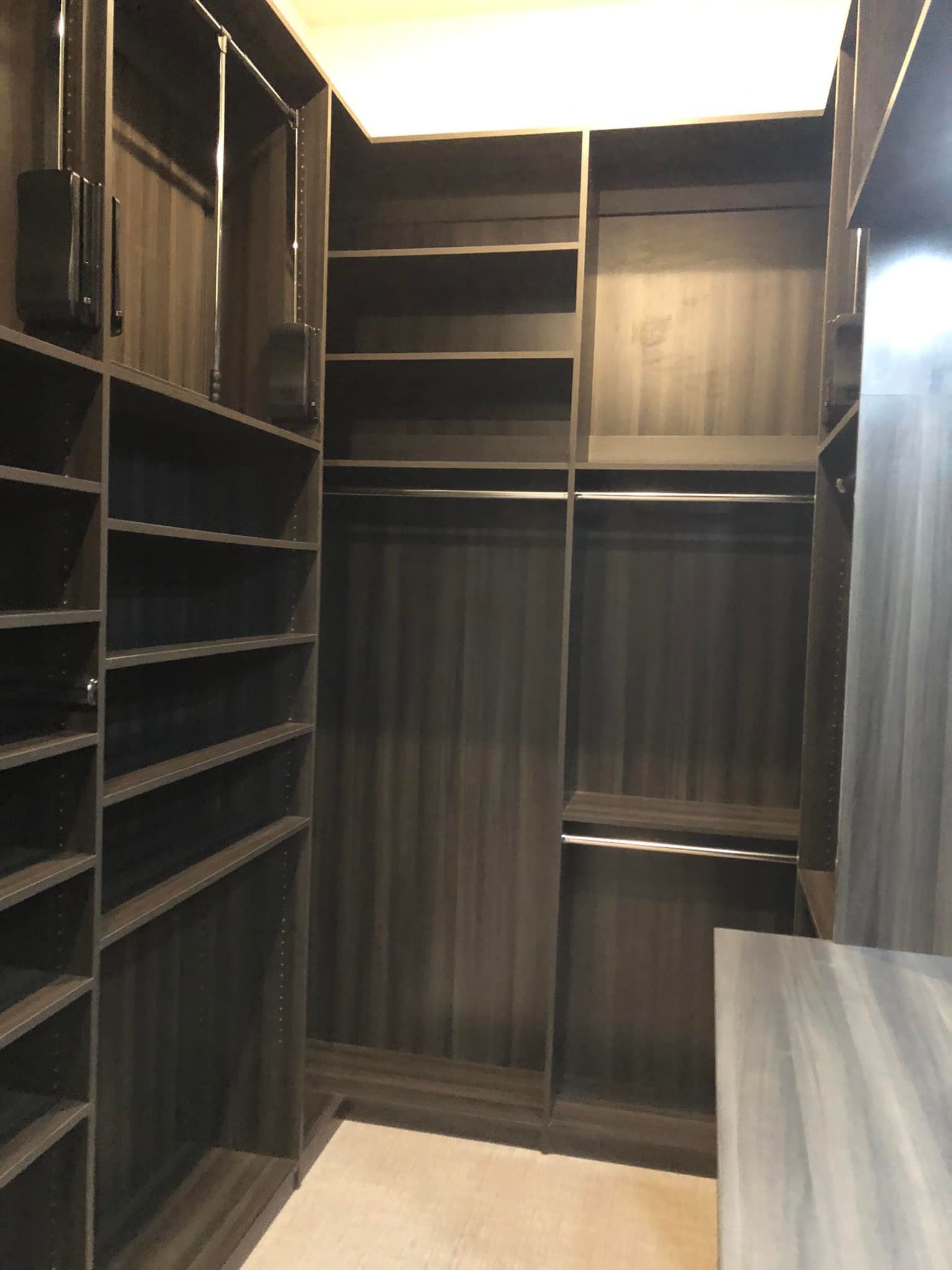Empty walk-in closet with dark shelving, hanging rods, and a light wood floor.