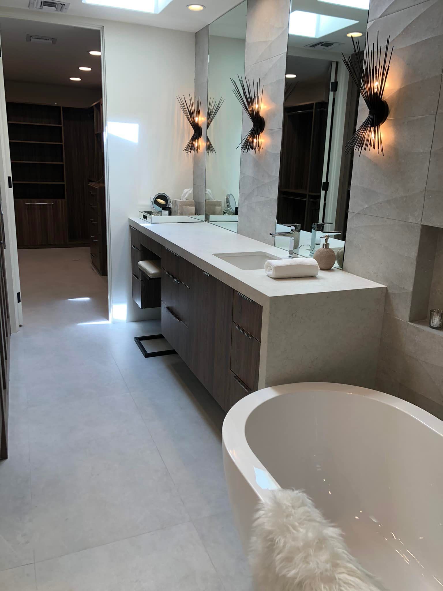Modern bathroom with long vanity, large mirrors, wall sconces, and a white freestanding tub