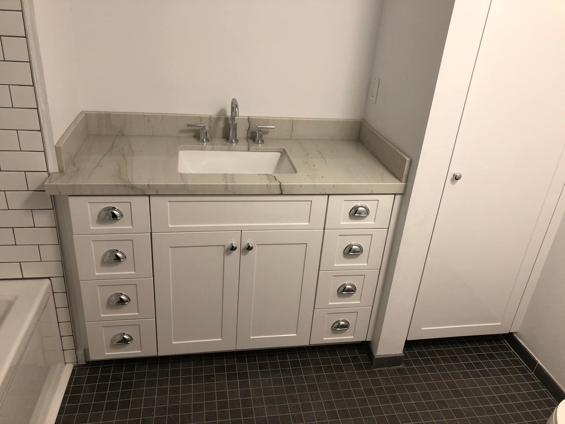 White bathroom vanity with sink, mirrorless wall, and dark tile floor